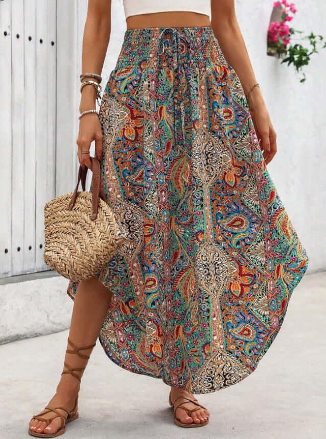 Boho ladies printed skirt with asymmetrical cut and colorful chevron pattern, styled with a straw bag and sandals.