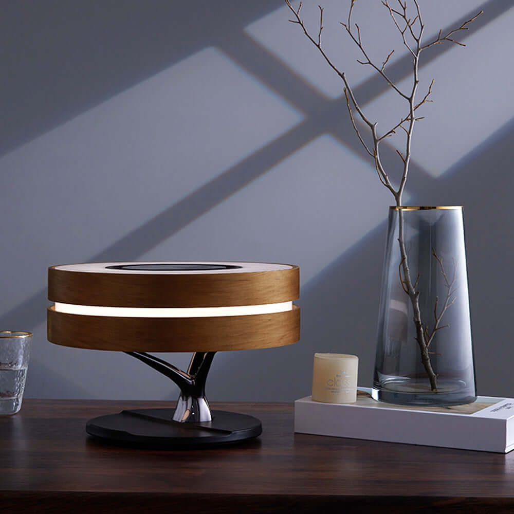 Modern All-in-One Intelligent Desk Lamp, Music Box, and Wireless Charger on a wooden desk next to minimalist decor.