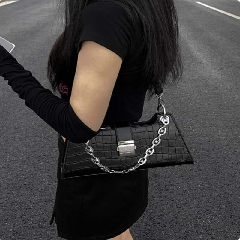 Stylish woman holding black faux leather baguette handbag with elegant chain detail, medium-sized and perfect for essentials.