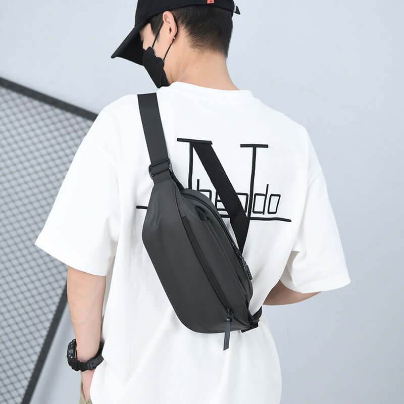High Capacity Waist Bag worn over the shoulder by a man in a white T-shirt; waterproof material; stylish and functional design.