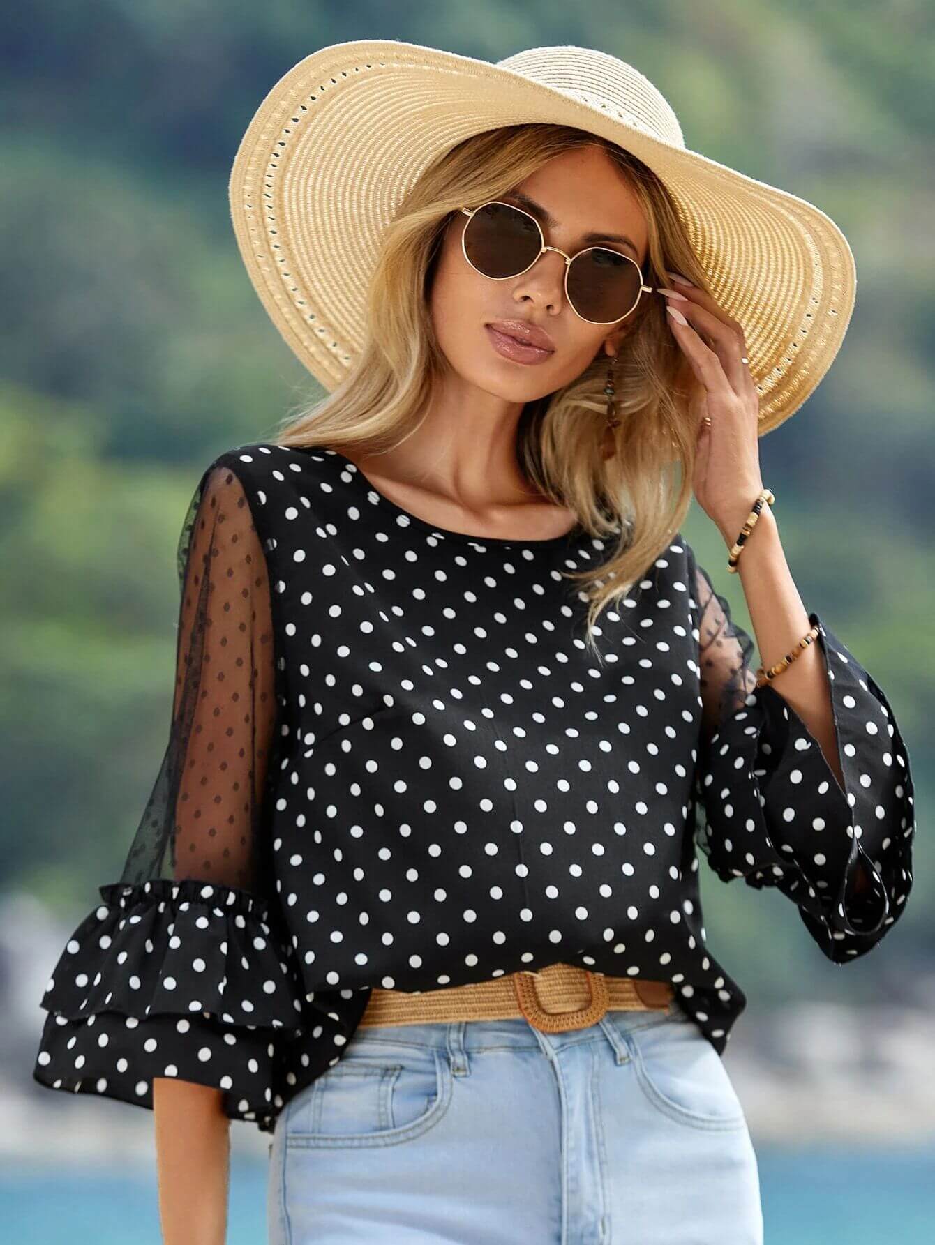 Woman wearing a Black Polka Dot Sheer Blouse with 3/4 bell sleeves, paired with a sunhat and sunglasses, showcasing stylish casual wear.