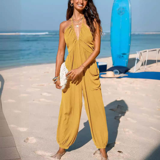 Woman wearing vibrant yellow Back Open Jumpsuit on a beach, accessorized with a white clutch, showcasing summer style and comfort.