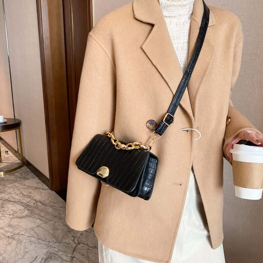 Woman holding a coffee cup wearing a beige coat with a black Crossbody Messenger Bag Purse, featuring a gold chain strap.