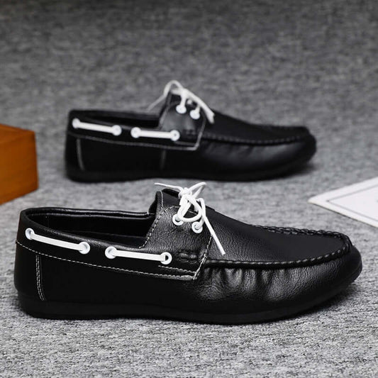Black faux leather loafers with white laces on a gray surface, showcasing elegant design and comfort.