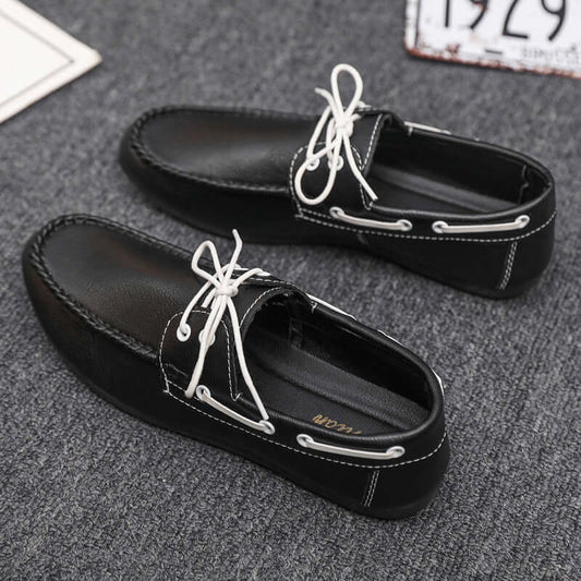 Black faux leather loafers with white laces on grey carpet, showcasing stylish design and comfort.