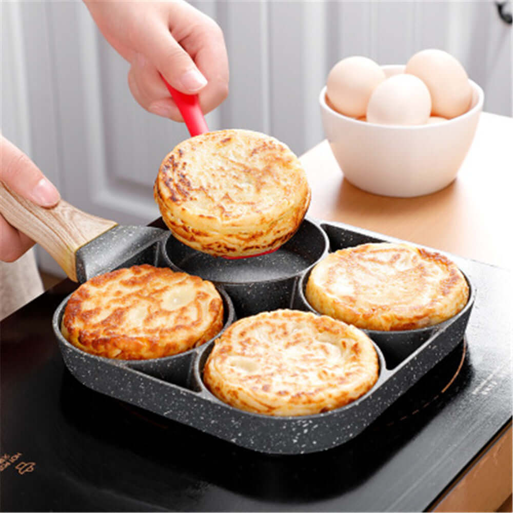 Four Hole Frying Pan in use, cooking pancakes with a hand lifting one out; eggs in background.