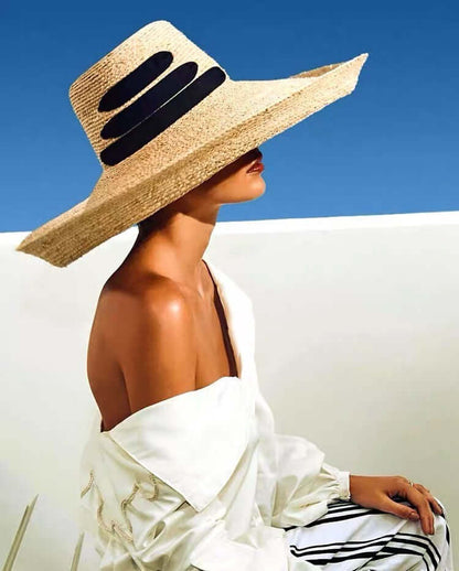 Model wearing a stylish Raffia Big Brim Hat against a blue sky, perfect for summer sun protection.